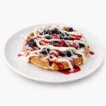 A golden Belgian waffle loaded with fresh strawberries, blueberries, blackberries, and a rich mascarpone cheese glaze at The Eggsquisite Cafe