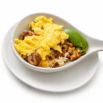 Chicken Carnitas Skillet at Eggsquisite Cafe with pulled chicken carnitas, corn, tomatoes, onions, jalapeños, cheese, avocado, and two eggs.