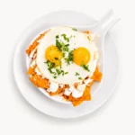 Chilaquiles at Eggsquisite Cafe with tortilla chips sautéed in homemade salsa and topped with crema, queso fresco, cilantro, onions, and eggs.
