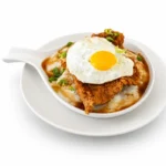 Spicy Chicken and Biscuits at Eggsquisite Cafe with fried chicken over biscuits and sausage gravy, topped with a sunny-side-up egg, chives, and hot honey.