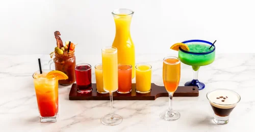 A refreshing iced brunch drink served in a vintage ribbed glass with fresh mint leaves and an orange slice on a bright yellow background at The Eggsquisite Cafe